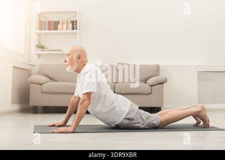 Senior Man Practicing Yoga on a Mat in a Living Room During the Afternoon Stock Photo
