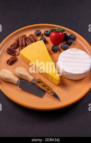 Cheese board presenting a selection of cheddar and brie cheeses, accompanied by fresh blueberries, strawberry, and pecans, perfect for an appetizer or Stock Photo
