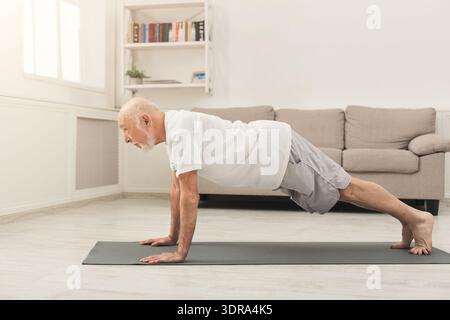 Older Man Doing Push-Ups on Mat in Living Room With Natural Light During Morning Hours Stock Photo
