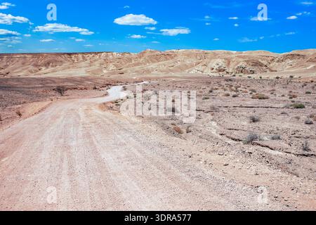 Winding dirt road through a vast desert landscape with rolling hills and blue sky Stock Photo