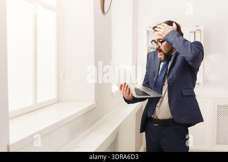 Businessman Reacts to Unexpected News While Using Laptop in Modern Office Setting Stock Photo