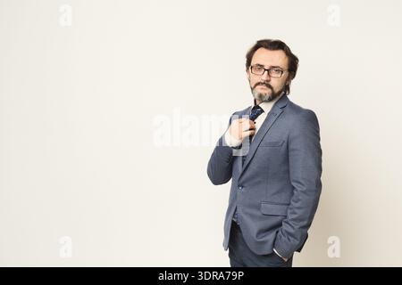 Man in Suit Adjusts Tie While Standing Against Plain Background in Studio Setting Stock Photo