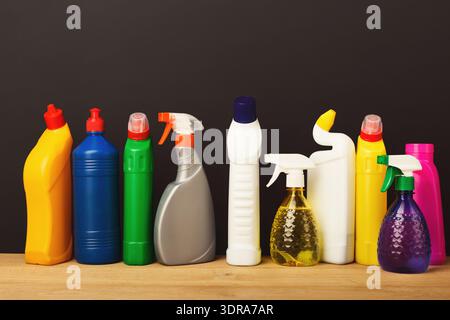 Collection of Cleaning Products Arranged in a Row on a Wooden Surface Against a Dark Background Stock Photo