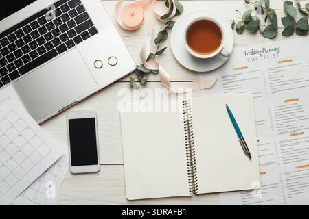 Collection of Wedding Planning Items on a Table With a Laptop, Planner, and Cup of Tea Stock Photo