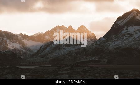 View of snow-dusted peaks pierce the heavens in a majestic display of nature's grandeur, bathed in the warm glow of the setting sun, Fredvang, Nordlan Stock Photo
