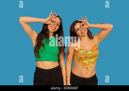 Two happy young women posing with an ok gesture over one eye Stock Photo