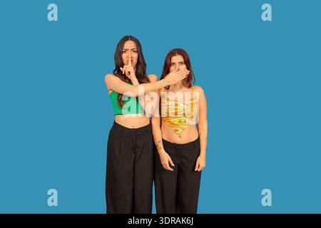 Woman putting finger on lips, silencing another woman covering her mouth, representing secrets Stock Photo