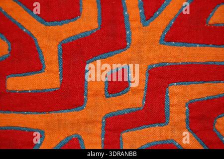 This early 20th-century mola panel is made of cotton with rectangles sewn together, cut out and appliquéd onto a blue backing printed with white dots. The appliqué design in red and orange depicts abstract forms. The panel demonstrates traditional Panamanian textile techniques, including layering and appliqué, with emphasis on geometric design, color, and decorative craftsmanship. Stock Photo