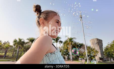 Girl playing outdoors surrounded by floating soap bubbles in warm golden sunlight. Stock Photo