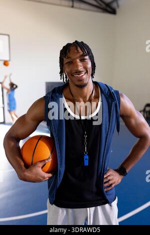 Holding ball and smiling confidently, male african American basketball coach in indoor court Stock Photo