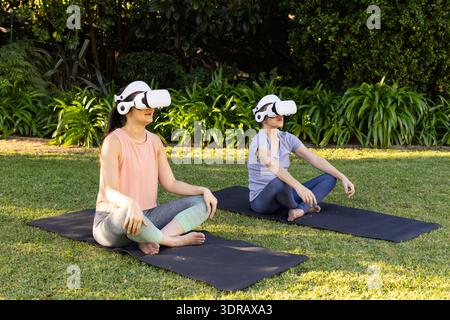 Practicing yoga outdoors, asian grandmother and granddaughter using vr headsets on mats in garden Stock Photo