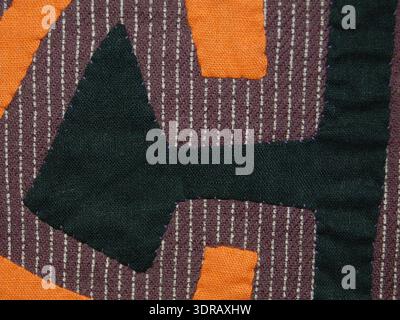 This early 20th-century mola panel is made from cotton, with rectangles sewn together and cut-out areas appliquéd. The grey cotton backing printed with white stripes supports a design appliquéd in orange and black, showing abstract geometric patterns. Tacking threads are still visible, illustrating the traditional Kuna layering and appliqué techniques, emphasizing bright color contrast, geometric motifs, and handcrafted textile artistry for cultural clothing. Stock Photo