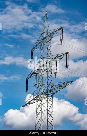 Power pole with high-voltage lines in portrait format with light cloud cover against a blue sky Stock Photo