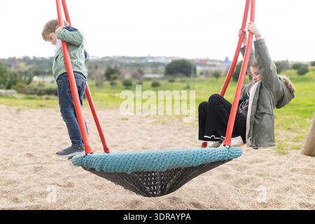 Children playing on nest swing at playground park Stock Photo