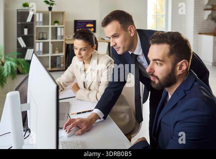 Business team analyzing data on computer in office, planning strategy together Stock Photo