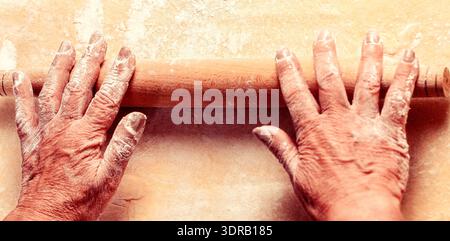 Dough with rolling pin. Woman old hands rolling out dough in flour with rolling pin in bakery Stock Photo