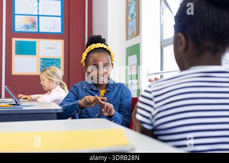 In school, african american girl using sign language to communicate with classmate in classroom Stock Photo