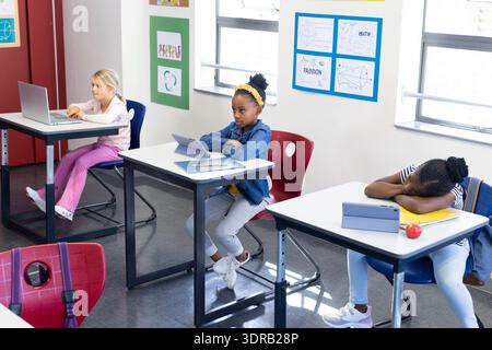 In school, multiracial girls using tablets and laptop in classroom, studying attentively Stock Photo
