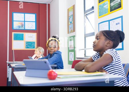 In school, multiracial girls using tablets and laptops while sitting at desks Stock Photo