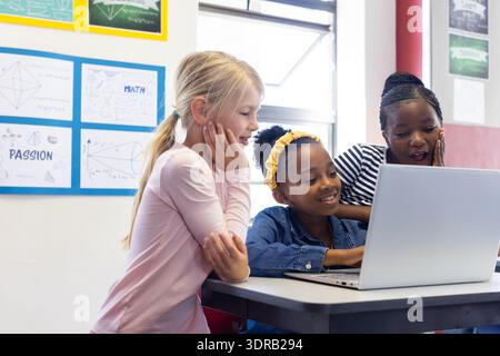 In school, three multiracial girls using laptop together in classroom, collaborating on project Stock Photo
