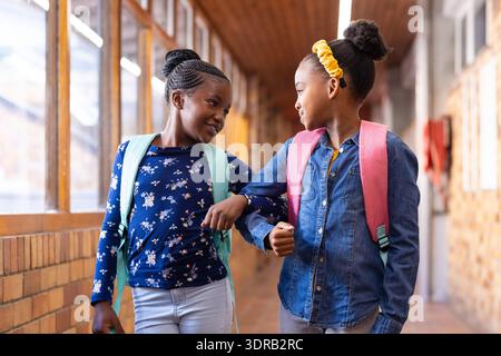 Walking in school hallway, two african american girls with backpacks smiling at each other Stock Photo