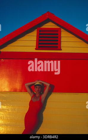 Young woman in pink dress standing in front of beach hut. Stock Photo