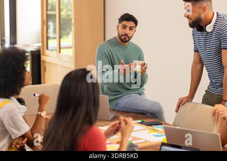 Discussing ideas, group of young friends collaborating with laptops and notes, start up business Stock Photo