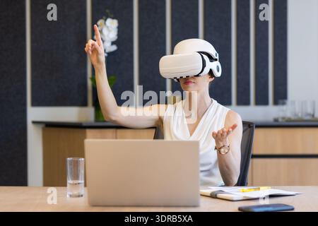 Using VR headset, businesswoman interacting with virtual interface in office meeting Stock Photo
