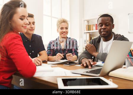 Group of Four People Engaged in Discussion While Working on a Laptop at a Table Stock Photo