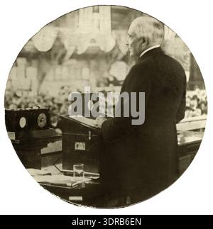 This image shows President Warren G. Harding (1865-1923) delivering a radio address in 1922. A crowd is visible in the background, slightly out of focus. The photograph represents early use of radio for presidential communication, public engagement through broadcasting, and technological adoption in political discourse. It highlights the intersection of media, governance, and public reception during the early 1920s in the United States. Stock Photo