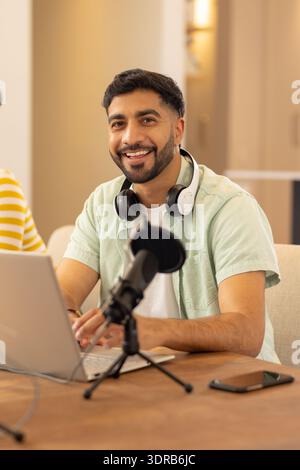 Using laptop and microphone, man smiling while working from home office Stock Photo