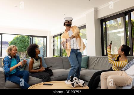 Using VR headset, young man entertaining diverse friends in living room, having fun Stock Photo