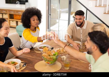 Sharing food and enjoying meal, young diverse friends gathering around dining table Stock Photo