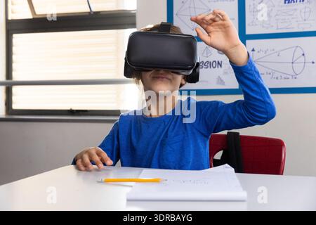 In school, boy using vr headset while sitting at desk with notebook Stock Photo