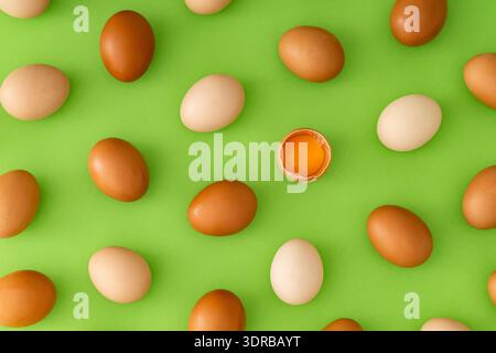 Food pattern made of natural fresh brown and white eggs with cracked egg and yolk on light green background. Creative food concept. Flat lay style. Stock Photo