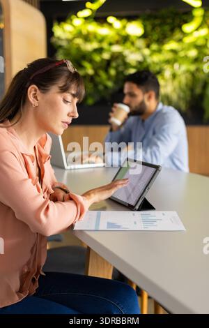 Using tablet for work, woman analyzing data while african american man working on laptop Stock Photo