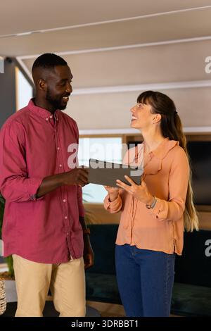 Discussing project details, colleagues using tablet and smiling in modern office Stock Photo