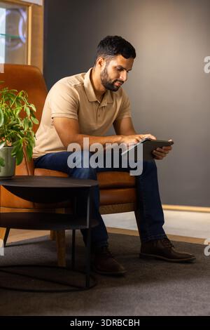 Using tablet, man sitting on chair and working in modern office Stock Photo
