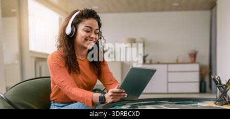 Young Woman Using Tablet at Home While Wearing Headphones During Daytime Stock Photo