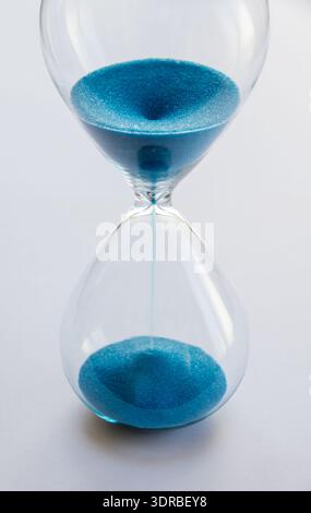 Hourglass containing blue sand isolated on white background Stock Photo