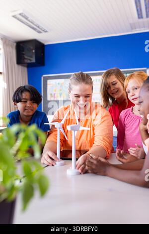 In school, female teacher and diverse students experimenting with wind turbine models in classroom Stock Photo