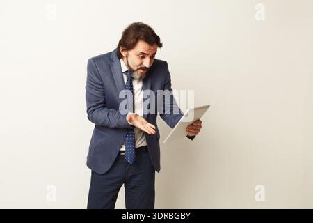 Man in Suit Looking Surprised While Holding Tablet in Office Setting Stock Photo