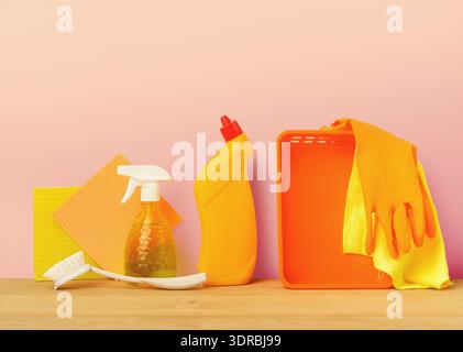 Cleaning Tools and Supplies Arranged on a Wooden Table Against a Pink Background Stock Photo