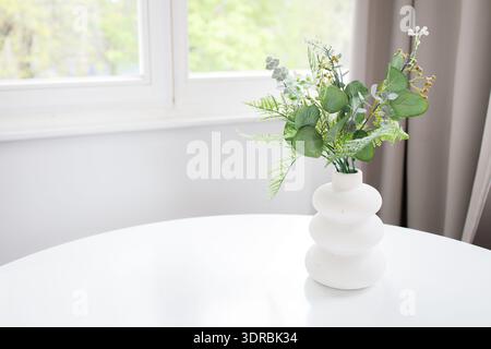 Minimalistic interior background with copy space: white table with artificial green plant in vase and window with soft morning light Stock Photo