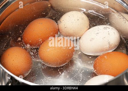 Eggs boiling in hot water closeup. Home cooking and food preparation process in kitchen. Simple everyday meal ingredient concept. Stock Photo
