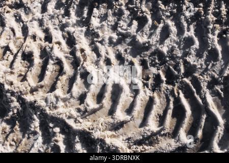 Tire tracks texture in dirty snow closeup. Winter road surface pattern. Mud and slush background during cold season outdoors. Stock Photo