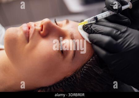 Female cosmetologist in transparent gloves makes an injection in the lower jaw of her client Stock Photo