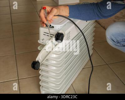 Close-up of man installing wheels on electric oil-filled heater. Home repair and heating system setup concept, solving heating issues during winter. Stock Photo