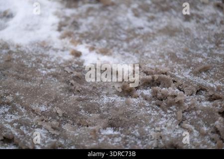 Close view of wet winter slush mixed with dirty snow and sand on an icy sidewalk. Urban seasonal texture showing thaw, melting snow, and slippery road Stock Photo