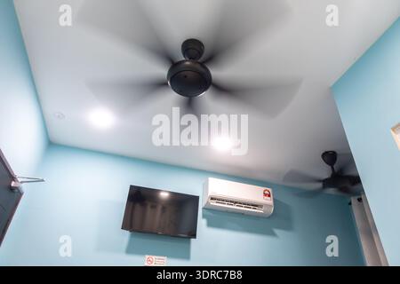 modern room interior featuring black ceiling fans and a wall-mounted air conditioner. The walls are painted in a light blue shade, flat screen tv Stock Photo